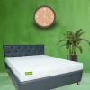 A mattress placed on a wooden frame, positioned in a cozy room with neutral decor and soft lighting.